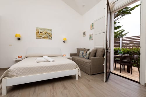 Bright bedroom with white bed, gray sofa, yellow lamps, and ocean views at Senia del Rais, Favignana