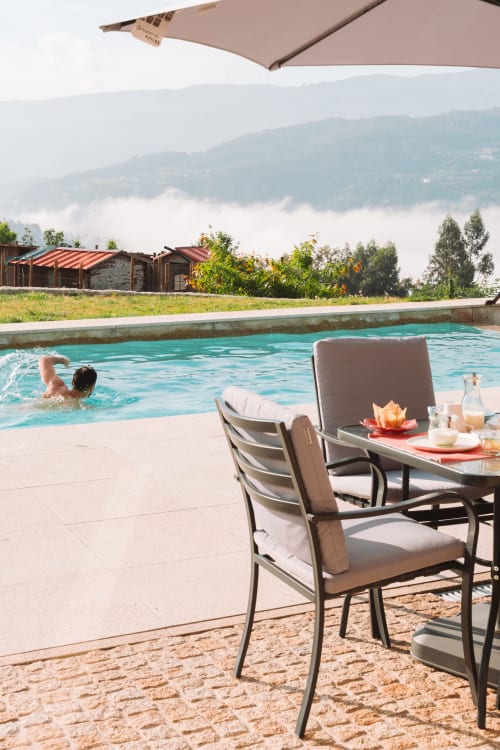 Beige lounge chairs and umbrella by turquoise pool at Canhoto Douro with misty Douro Valley mountains