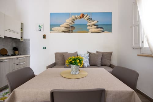 Dining area in Medusa apartment at Senia del Rais, Favignana, with table, chairs, sofa, and beach-themed wall art