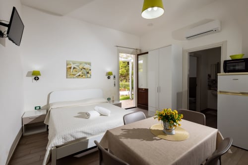 Medusa apartment at Senia del Rais, Favignana: bright studio with white bed, dining area, kitchenette, and garden view