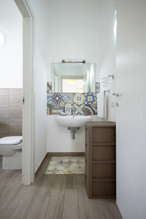 Modern bathroom in Medusa apartment at Senia del Rais, Favignana, with patterned tile backsplash, mirror, sink, and wooden