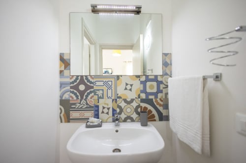 Modern bathroom with decorative patterned tilework, white sink, and lit mirror in Medusa room at Senia del Rais, Favignana