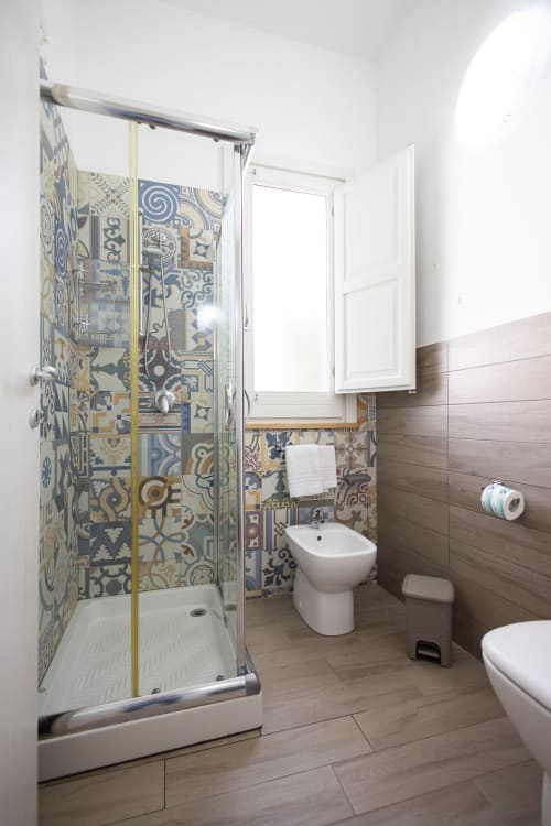 Modern bathroom with decorative blue and gold tile shower, white bidet and toilet, wood-look flooring at Senia del Rais