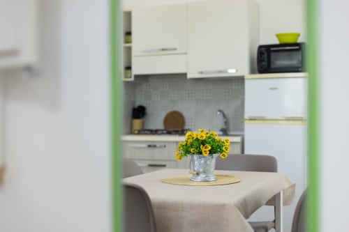 Bright dining area in Medusa apartment at Senia del Rais, Favignana, with yellow flowers on table and modern kitchen visible