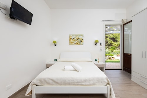 Bright bedroom with queen bed, garden view doors, TV, and modern amenities at Senia del Rais B&B in Favignana
