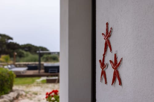 Red hand-painted figures on white wall at Senia del Rais B&B in Favignana with ocean view terrace beyond