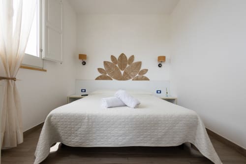 Bright bedroom with white bed, golden leaf headboard art, and window with ocean view at Senia del Rais, Favignana