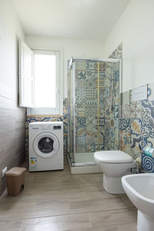 Modern bathroom at Senia del Rais in Favignana with patterned tile shower, white toilet, washing machine, and window