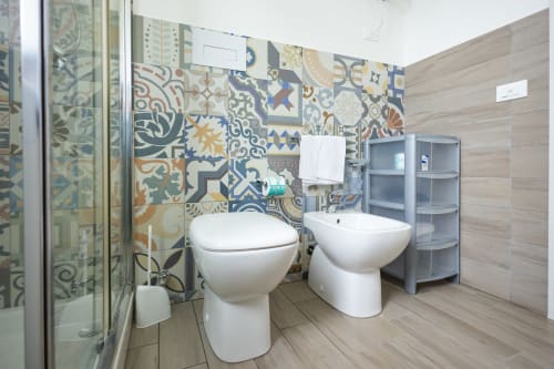 Modern bathroom at Senia del Rais in Favignana with colorful patterned tiles, dual white toilets, and wood accents