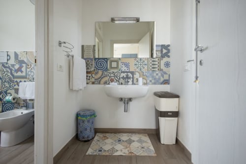 Modern bathroom at Senia del Rais in Favignana with patterned tile backsplash, wall-mounted sink, and mirror lighting