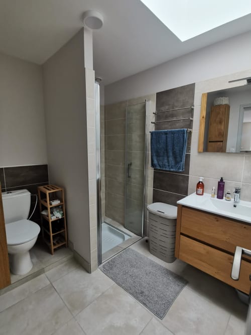 Salle de bains moderne du gîte La Belle Hélène avec douche à l'italienne, meuble vasque en bois, toilettes et puits de lumière à Bressuire