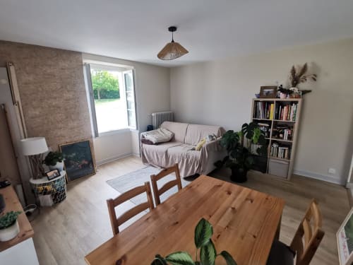 Séjour lumineux avec table en bois, canapé beige, bibliothèque et vue sur le jardin au Gite Natura Bella