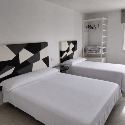 Habitación triple en Hostal Europa de Aldaia con dos camas, arte geométrico moderno en blanco y negro, y estantería blanca