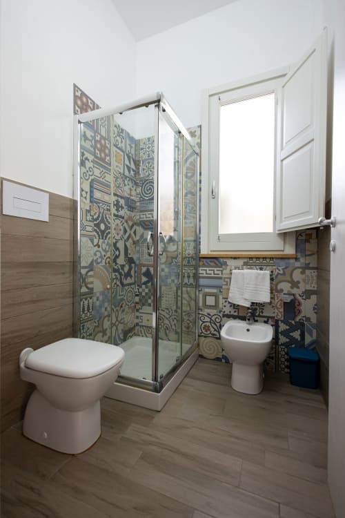 Modern bathroom in Tonno apartment at Senia del Rais, Favignana, featuring patterned tile shower enclosure, toilet, and bidet