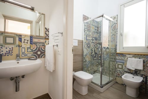 Modern bathroom at Senia del Rais in Favignana with patterned tiles, shower enclosure, sink, toilet, and bidet