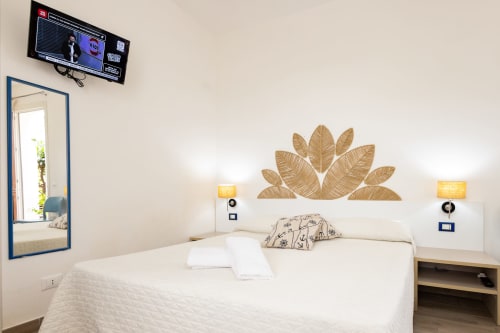 Bright modern bedroom at Senia del Rais in Favignana with white bed, golden leaf wall art, mirror, TV, and garden view