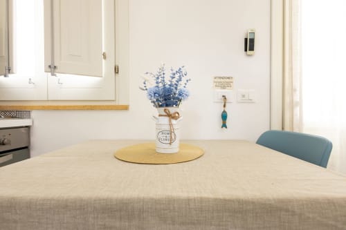 Modern kitchen with white cabinets, light wood dining table set with blue flowers, and teal chair at Senia del Rais apartment