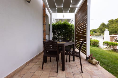 Covered outdoor dining patio with black chairs and table at Senia del Rais apartment in Favignana, overlooking garden