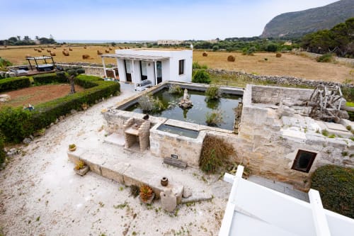 Senia del Rais room exterior in Favignana with modern white building, ancient stone ruins, pond, and rural Sicilian landscape