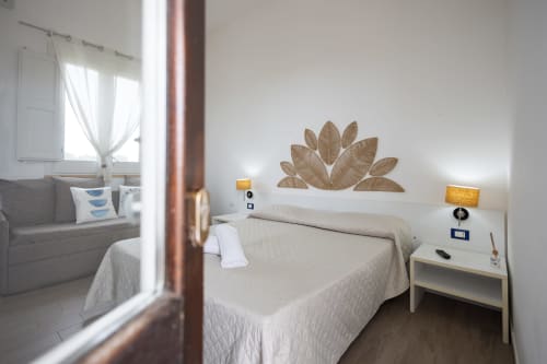 Bright bedroom in Corallo room at Senia del Rais, Favignana with sea view, queen bed, white nightstand, and woven leaf wall
