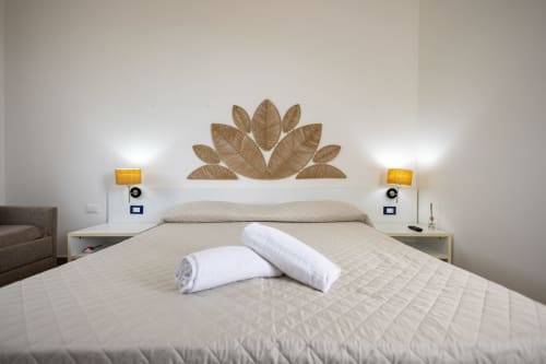 Bright bedroom at Senia del Rais in Favignana with white bedding, rolled towels, decorative leaf headboard art, and sea view