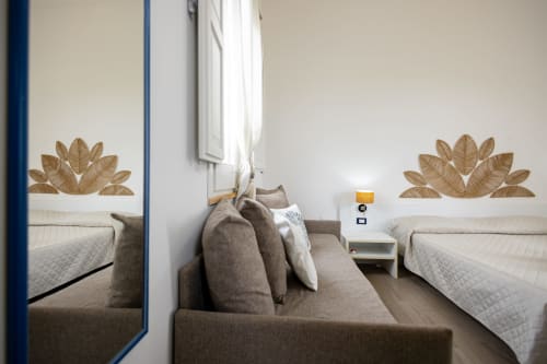 Modern twin bedroom at Senia del Rais in Favignana with gray sofa, white nightstand, and decorative leaf wall art