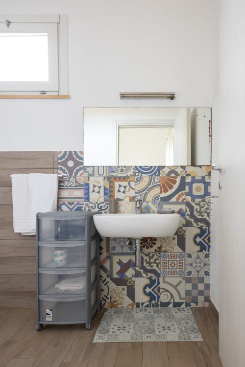 Modern bathroom sink with ornate blue and beige patterned tiles, mirror, and storage at Senia del Rais, Favignana
