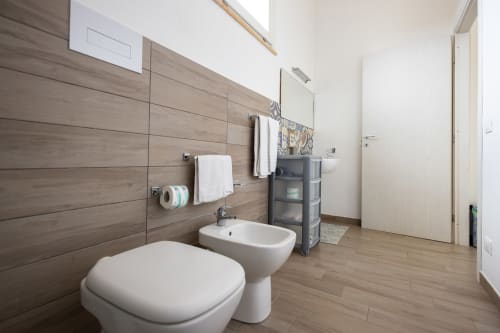 Modern bathroom in Corallo room at Senia del Rais, Favignana featuring toilet, bidet, sink, wood-tiled walls and towel racks