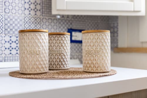 Three decorative ceramic canisters labeled Salt, Coffee, and Sugar on a woven placemat in the Sardina apartment kitchen at