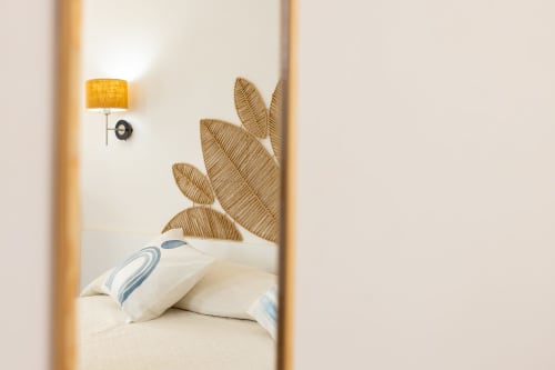 Cozy bedroom at Senia del Rais in Favignana with white pillows, woven leaf headboard, and yellow wall lamp