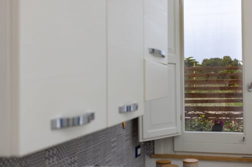 Modern kitchen with white cabinets and gray tile backsplash overlooking garden at Senia del Rais, Favignana