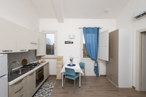 Modern kitchen-dining area in Sardina apartment at Senia del Rais, Favignana with blue chairs, white cabinetry, and mountain
