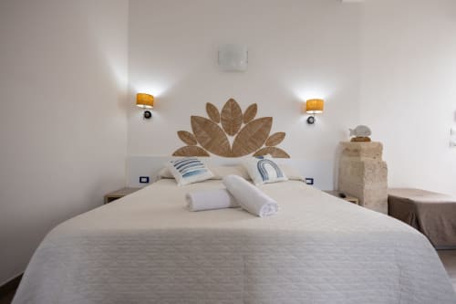Bright bedroom at Senia del Rais in Favignana with double bed, decorative leaf headboard, striped pillows, and modern wall