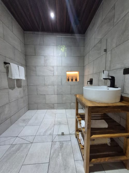 Baño moderno en Habitación Morpho de Fauna Lodge con lavabo redondo, vanitory de madera y ducha walk-in amplia en tonos grises