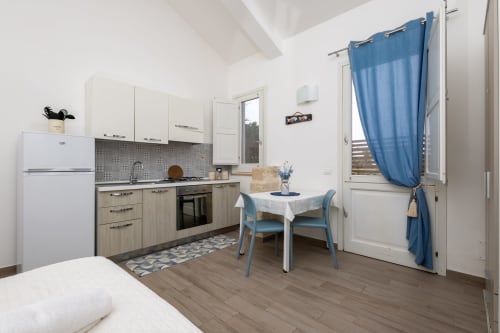 Modern studio apartment in Favignana with kitchenette, dining table, blue chairs, and mountain view through doors