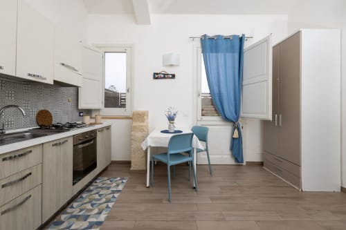 Sardina apartment kitchen-dining area in Senia del Rais, Favignana with blue chairs, white table, and mountain view access