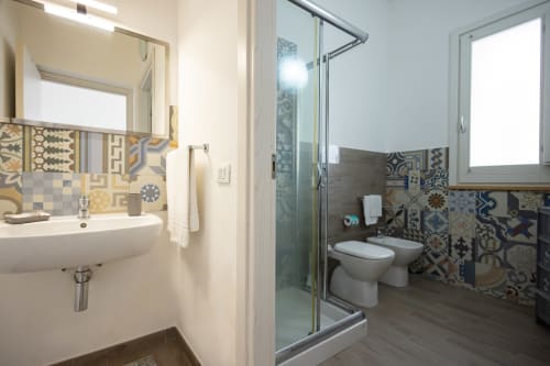 Modern bathroom in Sardina apartment at Senia del Rais, Favignana with patterned tile backsplash, glass shower, and white