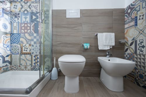 Modern bathroom in Sardina apartment at Senia del Rais, Favignana with toilet, bidet, sink, patterned tiles, and shower area.