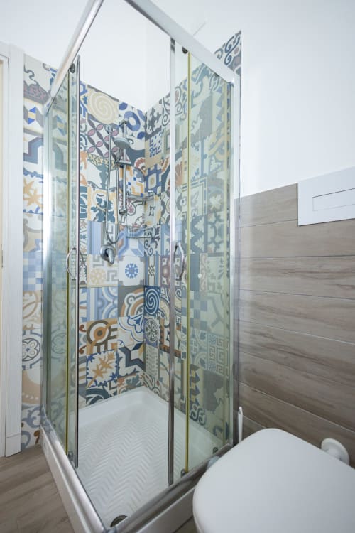 Modern glass shower enclosure with colorful patterned tile walls in Sardina apartment at Senia del Rais, Favignana