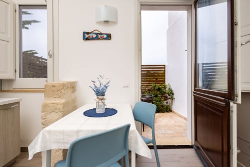Bright dining area in Sardina apartment at Senia del Rais, Favignana, with blue chairs, white tablecloth, and access to