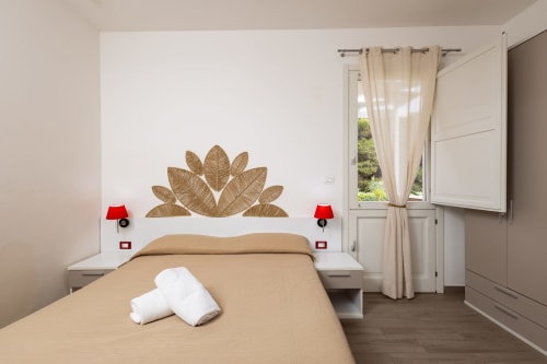 Bright modern bedroom at Senia del Rais in Favignana with beige bedding, golden leaf headboard art, red lamps, and ocean view