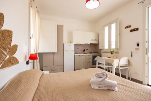 Tartaruga Marina apartment bedroom with kitchen area, double bed with towels, dining table, and ocean view in Favignana,