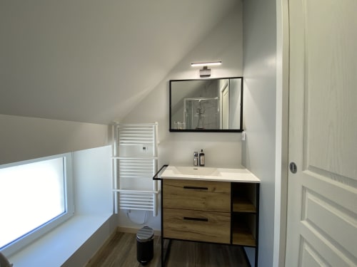 Modern bathroom in Domaine des Piéris cottage with wooden vanity, mirror, heated towel rail, and window view