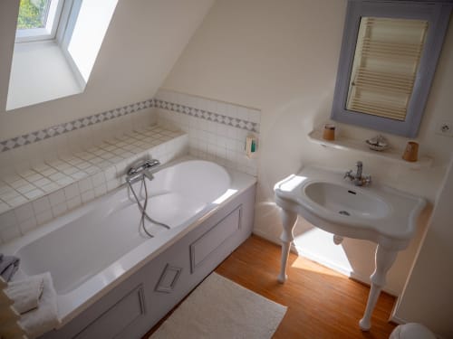 Bright attic bathroom in Chambre Ivoire at Ferme De La Sensee with bathtub, pedestal sink, and skylight