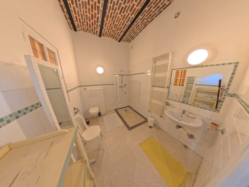 Spacious accessible bathroom at Ferme De La Sensee with walk-in shower, sink, toilet, yellow bath mat and bright ceiling