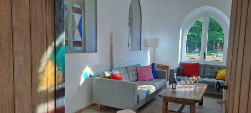 Salon moderne de la villa La Chapelle au Château de la Malmaison avec canapés gris, coussins colorés et fenêtres cintrées