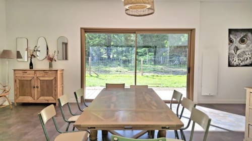 Salle à manger contemporaine au Château De La Malmaison avec table en bois, chaises vertes et grandes portes vitrées donnant sur la piscine