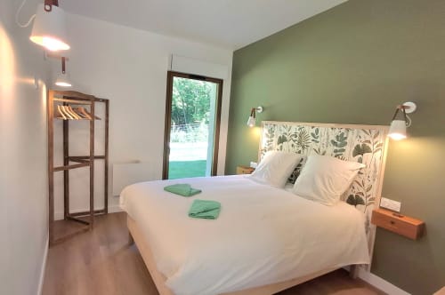 Chambre moderne au Château De La Malmaison en Champagne avec mur d'accent vert, lit blanc et vue sur la piscine depuis les portes vitrées