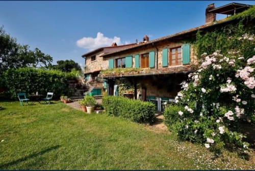 Rustieke Toscaanse villa bij Podere di Maggio B&B met stenen gevel, groene luiken, bloeiende tuinen en verzorgde gazon