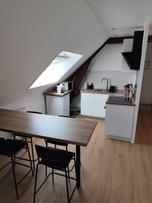 Cuisine et salle à manger modernes du studio mansardé d'Accolade Châteaudun avec plafond en pente, mobilier blanc et vue sur la ville